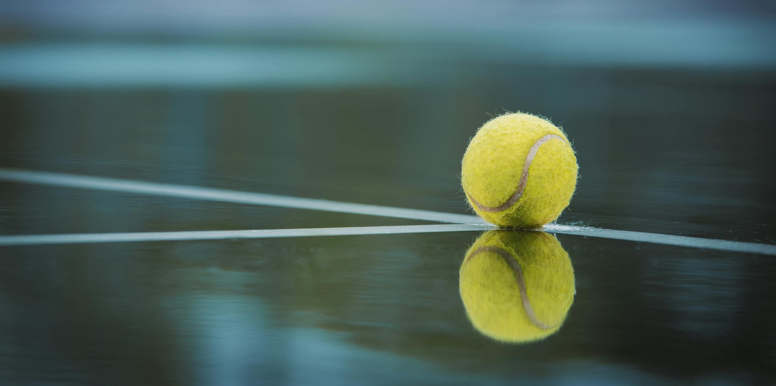 Photo of yellow tennis ball on stadium court's white line marking